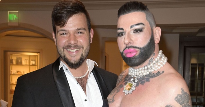 Ein junger Mann mit einer Perlenkette und ein Mann mit Bart und rosa Lippenstift.