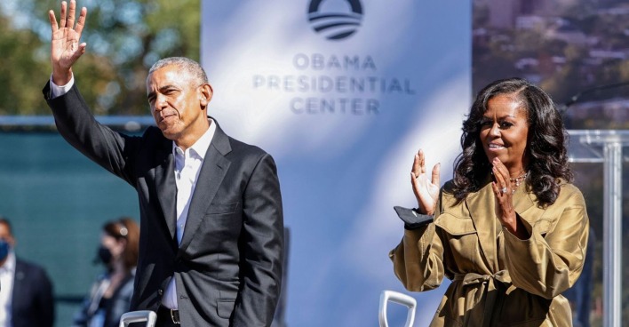 Barack und Michelle Obama klatschen und winken bei einer Veranstaltung.
