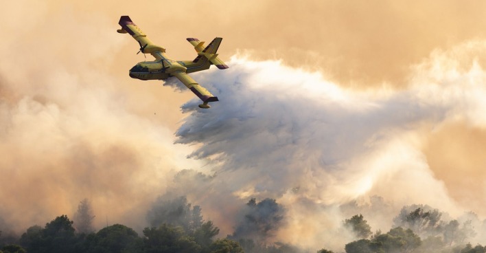 Ein Löschflugzeug leert seinen Wassertank über der brennenden Insel