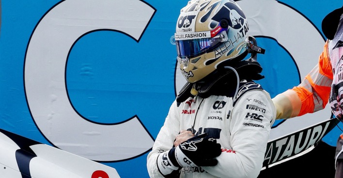 Ricciardo mit Helm und in Rennmontur neben der Strecke. Er hat einen Handschuh ausgezogen und hält sich die linke Hand.