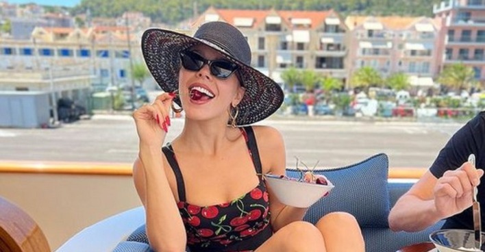 Victoria Swarovski mit Sonnenhut auf einer Yacht, sie isst eine Kirsche.