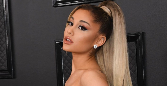 Ariana Grande auf dem roten Teppich vor einer schwarzen Tür mit zusammengebundenen, blonden Haaren.
