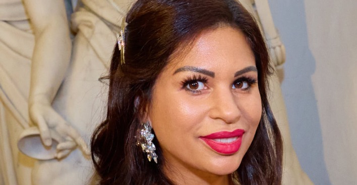 Nina Bambi Bruckner vor einer weißen Statue mit pinken Lippenstich und großen Ohrringen.