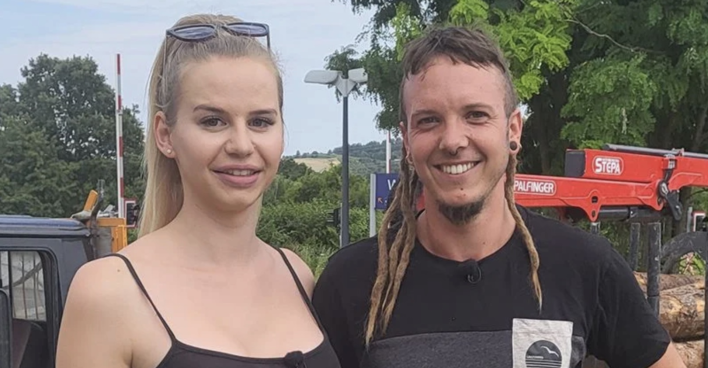 Eine blonde Frau und ein Mann mit Dreadlocks am Land vor einem Traktor.