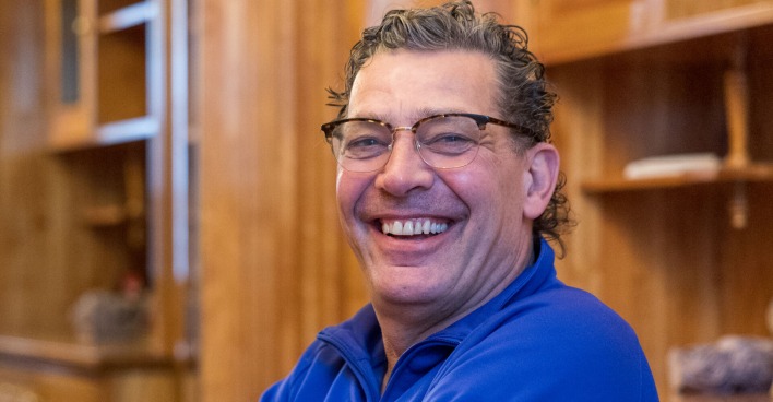 Schauspieler Gregor Blóeb mit einem blauen Hemd vor einer Holzwand.