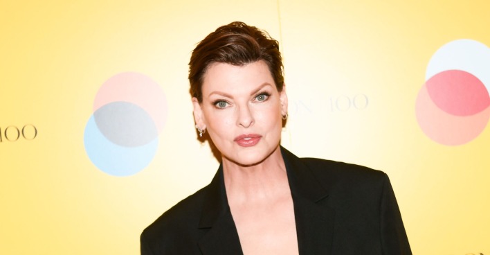 Linda Evangelista mit kurzen Haaren und einem schwarzen Anzug vor einer gelben Wand
