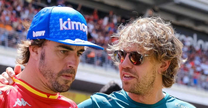 Alonso im Alpin und Sebastian Vettel im Aston Martin-Dress, sprechend auf der Rennstrecke.