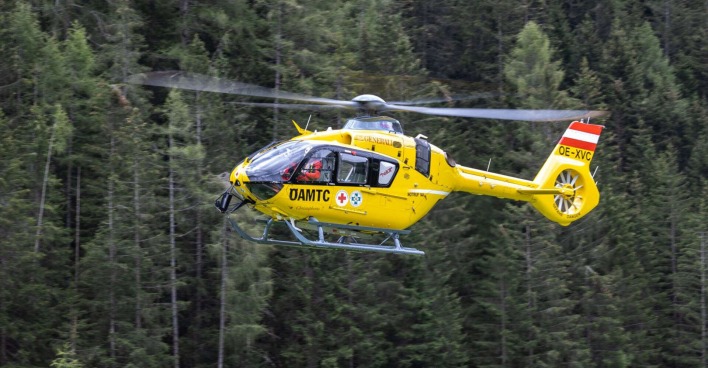 Der gelbe ÖAMTC-Hubschrauber fliegt in einem Waldgebiet.