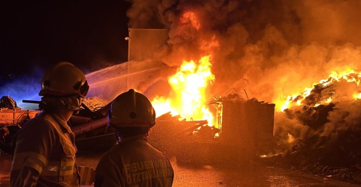 Zwei Feuerwehrleute blicken in die Flammen.