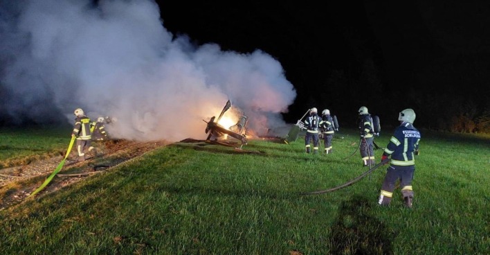 Feuerwehrmänner versuchen einen brennenden Hubschrauber auf einem Feld zu löschen.