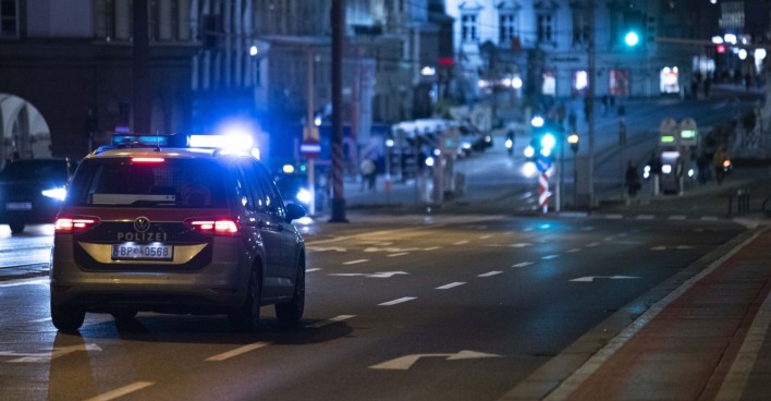 Ein Polizeiauto fährt mit Blaulicht nachts über die Straße.