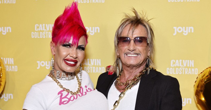Gina trägt einen pinken Irokesen und ein weißes T-Shirt mit einer Aufschrift "Barbie". Bert Wollersheim hat blonde Haare und eine verdunkelte Sonnenbrille.