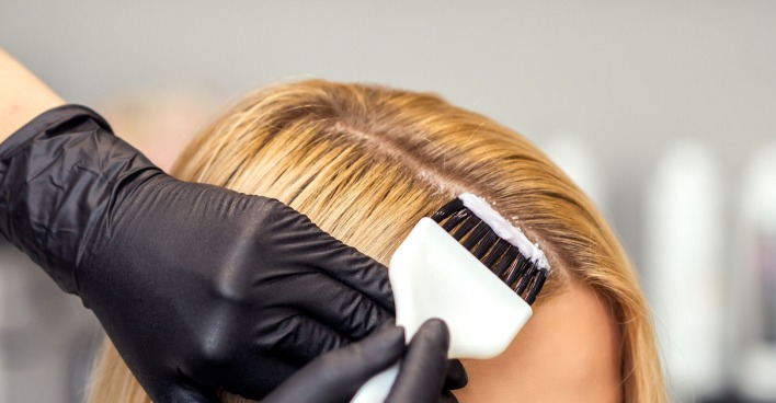 Der dunkle Ansatz eines blonden Haarschopfes wird nachgefärbt.