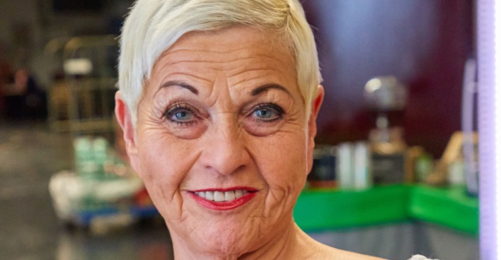 Eine Dame reifen Alters mit einem pinken Lippenstift und sehr kurzen blonden Haaren.