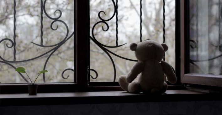 Ein einsamer Teddybär sitzt vor einem düsteren Fenster.