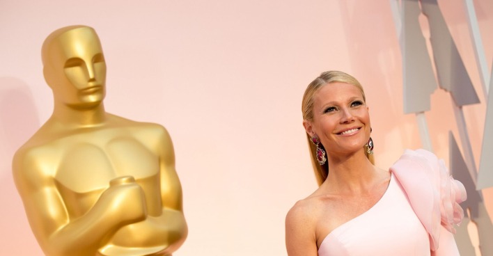 Gwyneth Paltrow in einem rosa Kleid neben einer Oscarstatue