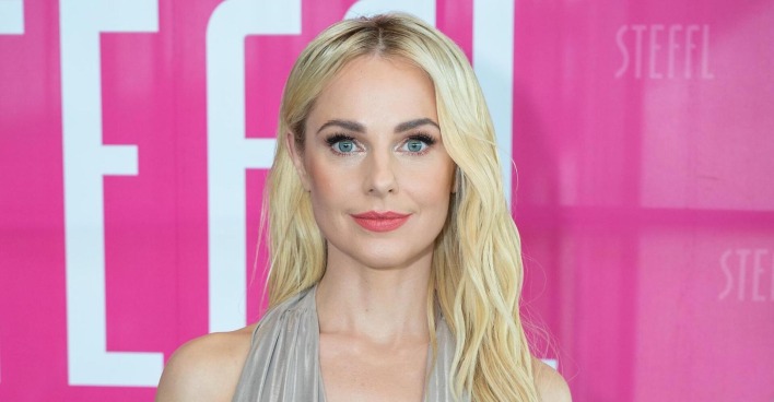 Silvia Schneider mit offenen blonden Haaren vor einer pinken Fotowand.