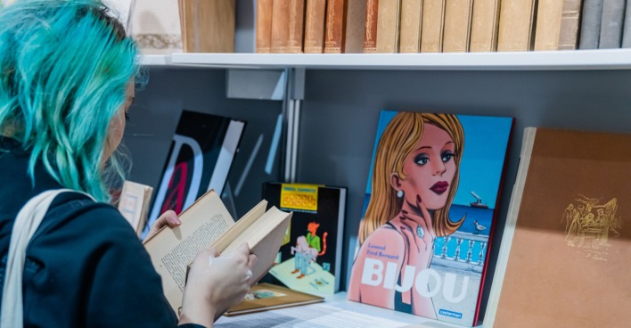 Junge Frau mit blauen Haaren in einem Buch blätternd, von hinten