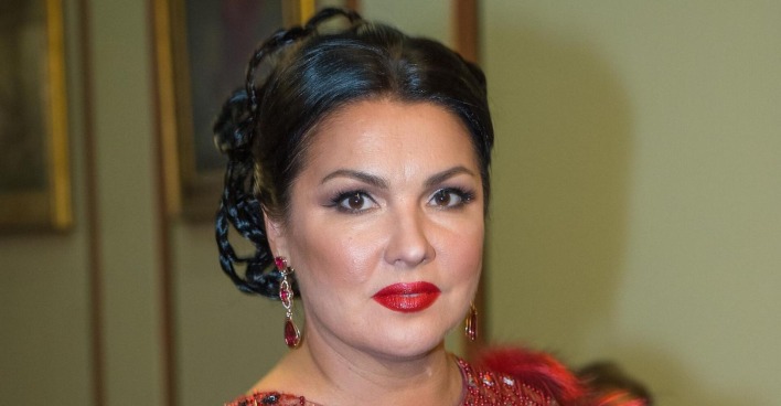 Anna Netrebko trägt hochgesteckte schwarze Haare, stark geschminkte Augen und einen roten Lippenstift.