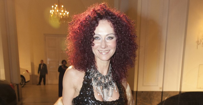 Christine Lugner trägt offene violette Haare und eine prunkvolle Kette. Dazu ein elegantes schwarzes Kleid, das glitzert.