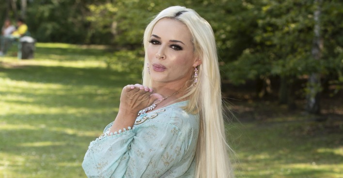 Daniela Katzenberger wirft der Kamera einen Kuss zu. Sie steht in einem hellen Sommerkleid auf einer Wiese.