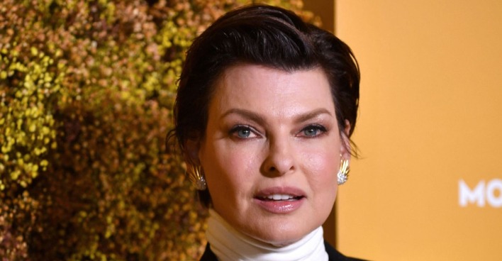 Linda Evangelista trägt einen weißen Rollkragenpullover und kurze zurück gegelte braune Haare.