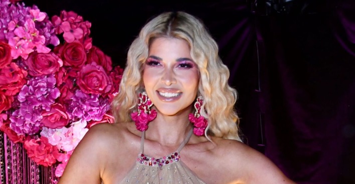 Micaela Schäfer mit offenen blonden Haaren vor einer Wand aus Rosen.