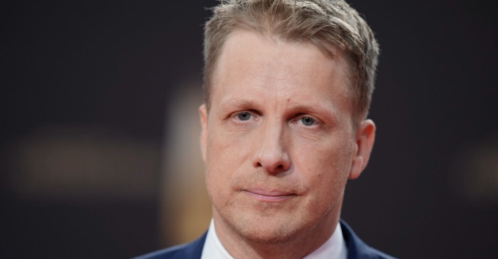 Oliver Pocher trägt einen dunklen Anzug. Er hat kurze blonde Haare und einen traurigen Blick.