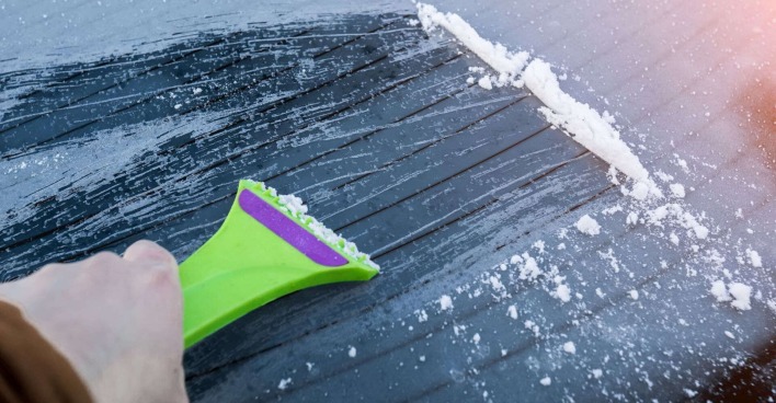 Eis wird mit einem Eiskratzer von der Scheibe entfernt.