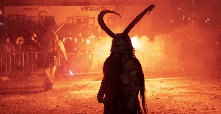 Ein Krampus steht vor dem Publikum, hinter ihm Feuer.