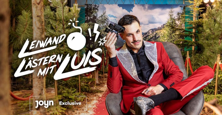 Luis mit einem roten Anzug und einem schwarzen Hemd. Er hält ein Fernglas in der Hand.