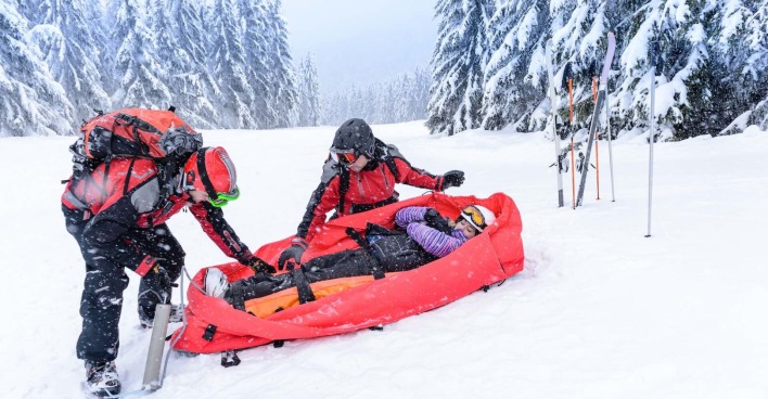 Zwei Rettungskräfte bergen einen verletzte Person auf der Piste.