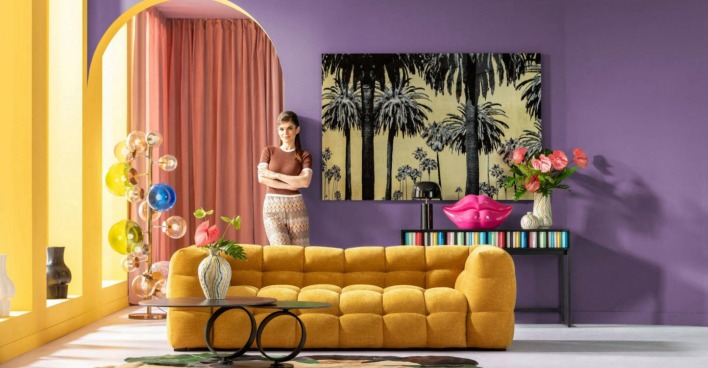 Wohnzimmer mit senffarbener Couch, lila wand, Frau im Hintergrund
