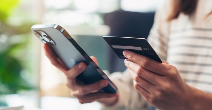 Eine Frau hält in einer Hand ein Smartphone und in der anderen eine Bankkarte.