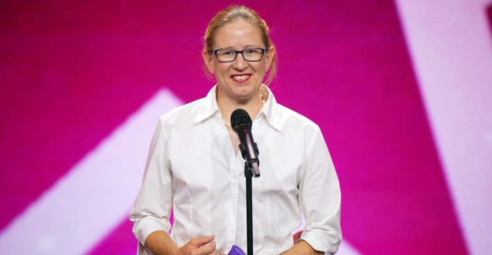 Die australische "Das Supertalent" Teilnehmerin Beatrice McQueef steht vor einem Mikrofon und trägt ein weißes Hemd. Hinter ihr ist eine pinke Fotowand.