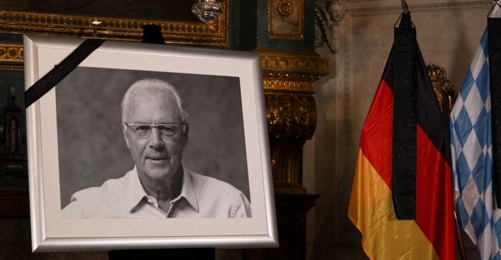 Ein Schwarzweißfoto des verstorbenen Franz Beckenbauer neben einer Deutschlandfahne.