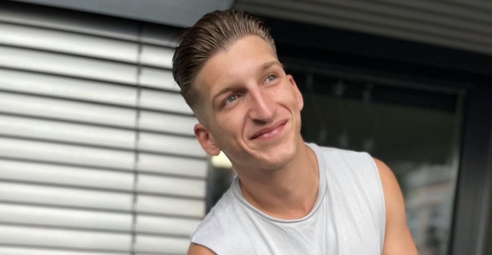 Satans Bratan grinst und trägt ein hellgraues T-Shirt.