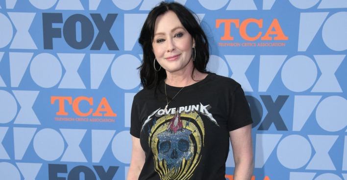 Shannen Doherty vor einer Fotoleinwand mit einem schwarzen T-Shirt.