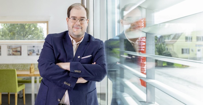Yves Suter, GF Hartl Haus, lehnt sich an eine Glaswand | Credit: Julia Dejmek
