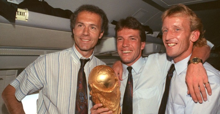 Andreas Brehme hält mit Lothar Matthäus und Franz Beckenbauer den WM-Pokal