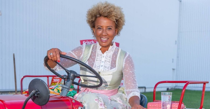 Arabella Kiesbauer im Dirndl auf einem Traktor.