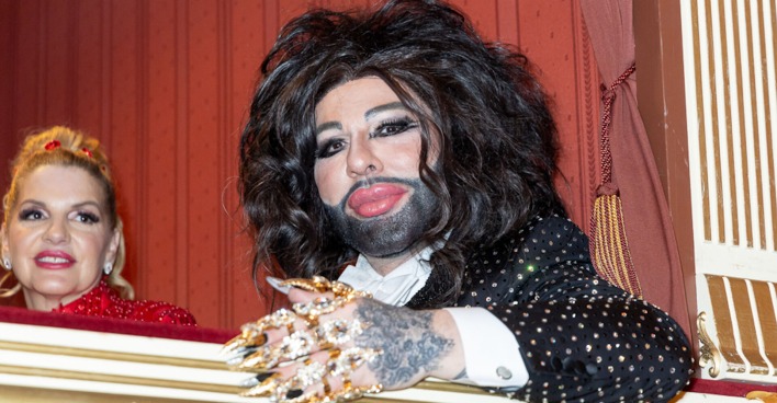 Harald Glööckler mit viel goldenen Schmuck und langen schwarzen Haaren auf dem Opernball 2024.