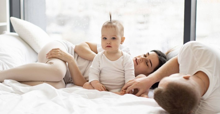 Paar mit Baby, das nicht schlafen will und kerzengerade auf dem Bett sitzt.