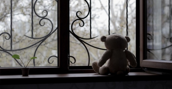 Ein einsamer Teddybär sitzt vor einem vergitterten Fenster.