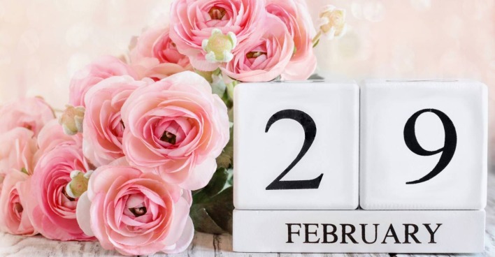 Übereinander gestapelte weiße Holzklötze, die zusammengesetzt den "29. Februar" ergeben, verziert mit rosa Rosen.