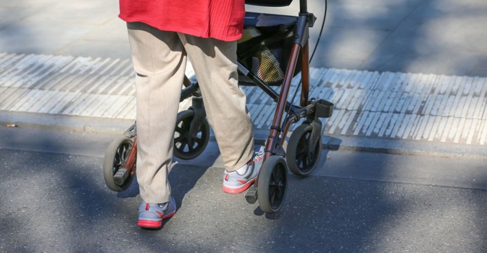 Eine Frau ist mit einem Rollator unterwegs.