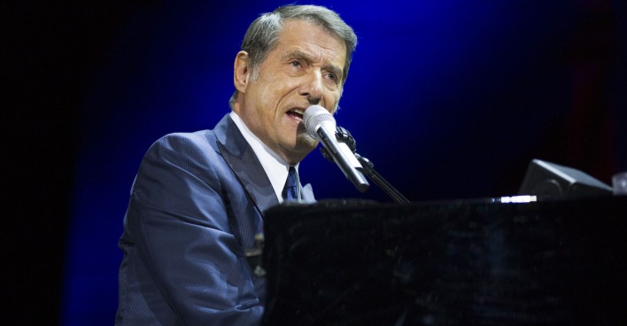 Udo Jürgens singt auf einer Bühne und spielt dabei auf einem Klavier.