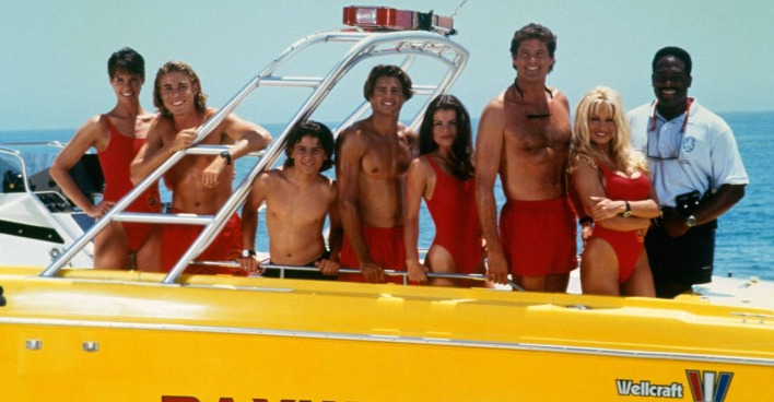 Das Baywatch-Ensemble, das in einer Reihe auf einem gelben Motorboot posiert
