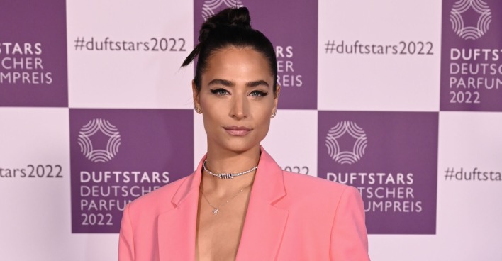Amira Pocher mit geschlossenen schwarzen Haaren und einem rosa Outfit.