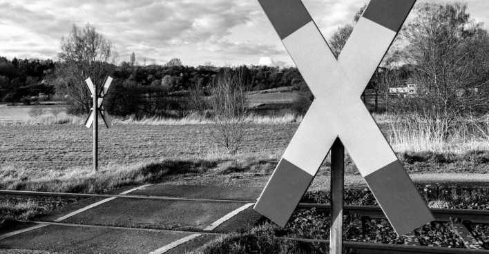 Ein düsteres Schwarz-weiß-Bild von einem Bahnübergang mit Andreaskreuz.